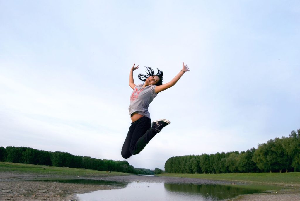 Happy woman jumping outdoors by a lake, enjoying freedom and nature.